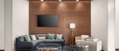 Una sala de estar moderna con un sofá gris curvo, una mesa de centro redonda, una lámpara de pie y un televisor montado en una pared con textura.