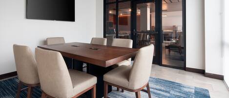 A conference room with a large table, six chairs, a flat-screen TV, and a blue patterned carpet.