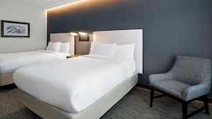 Una habitación de hotel con dos camas, un sillón gris y una lámpara fijada a la pared.