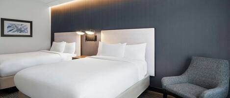 Ein Hotelzimmer mit zwei Betten, einem grauen Sessel und einer Wandleuchte.