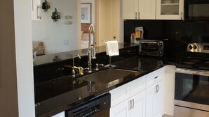 A modern kitchen with a black countertop, stainless steel appliances, white cabinets, and a visible door leading to another room.
