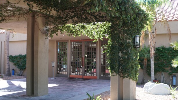 A building entrance with a glass door, surrounded by a gravel area and plants.