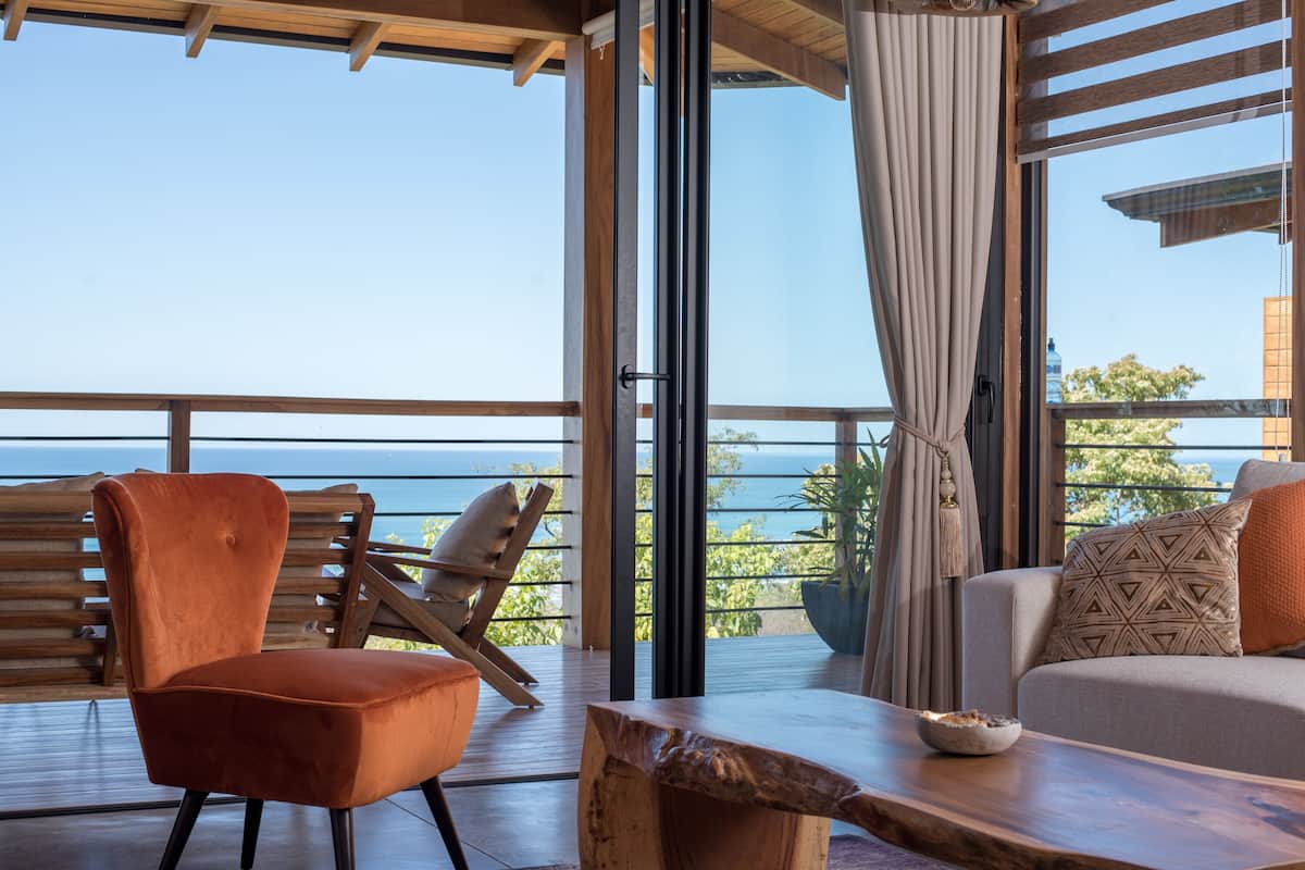 Una habitación moderna con suelo de madera, un sofá, una silla y vista al mar.