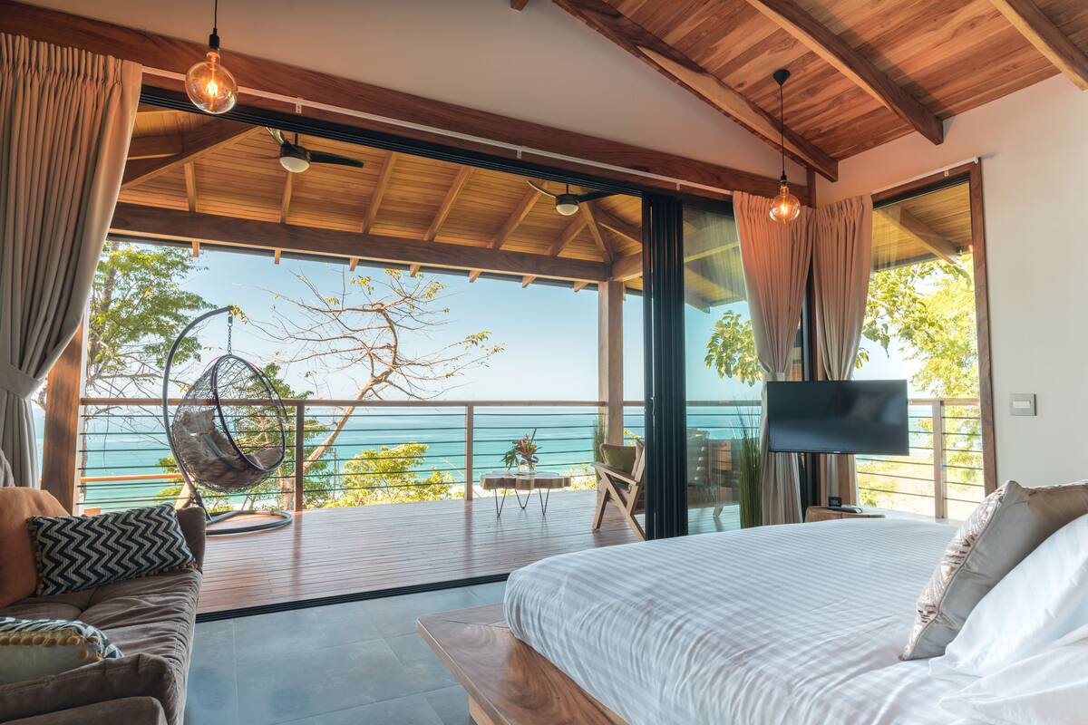 Un dormitorio con una cama grande, televisor y vista al océano.