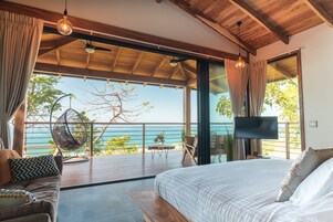 Un dormitorio con una cama grande, televisor y vista al océano.
