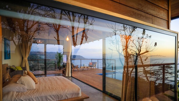 Een moderne slaapkamer met een groot bed, een houten terras en uitzicht op zee.