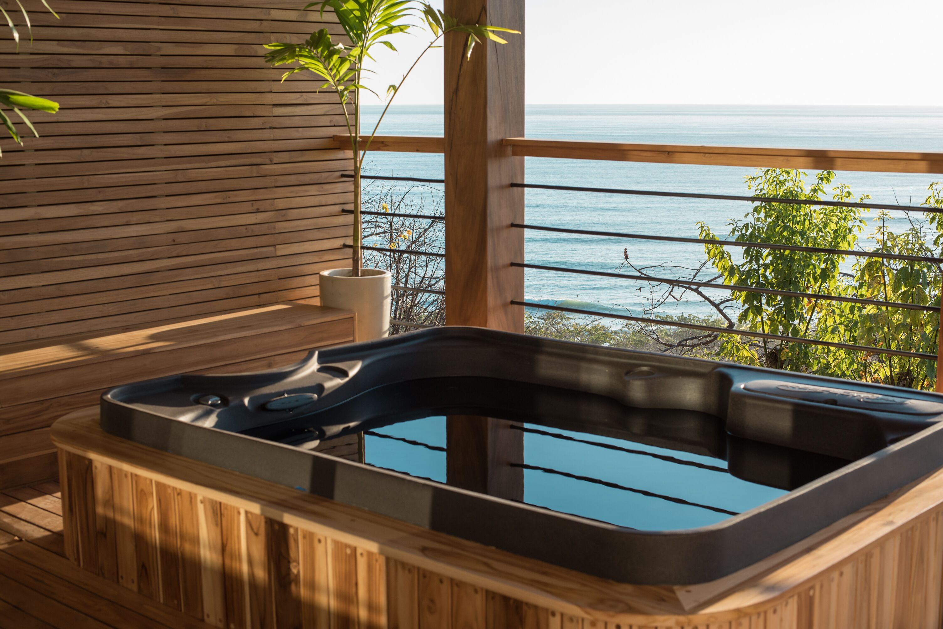 Una bañera de hidromasaje de madera con revestimiento de vidrio, con vistas a una masa de agua.