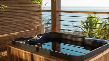 Una bañera de hidromasaje de madera con revestimiento de vidrio, con vistas a una masa de agua.