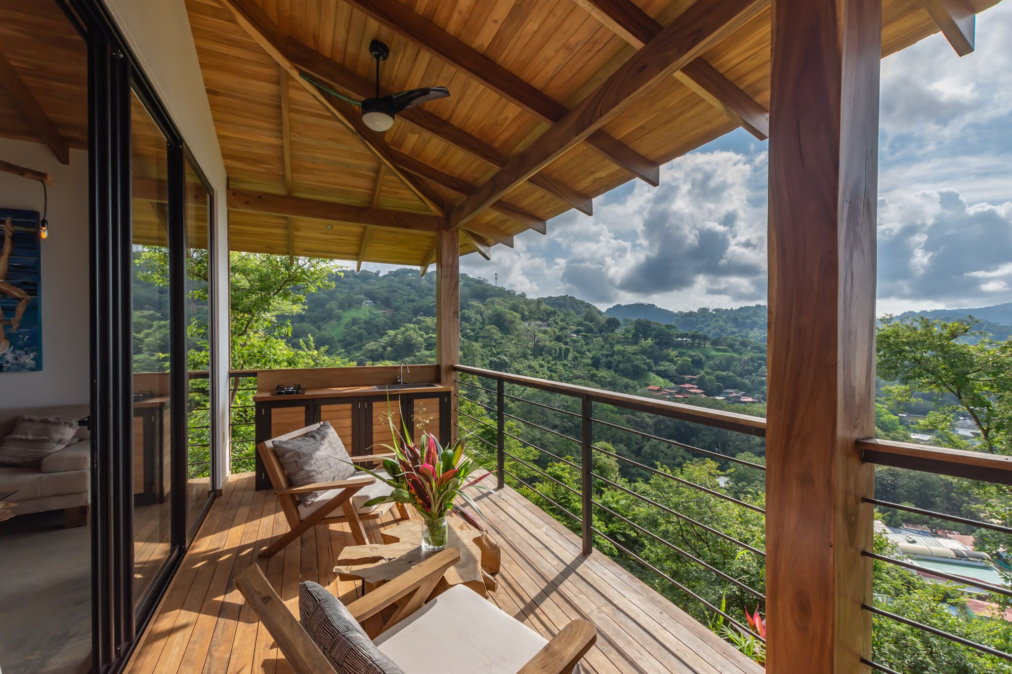 Una terraza de madera con un sofá y una mesa, con vistas a un paisaje verde exuberante.
