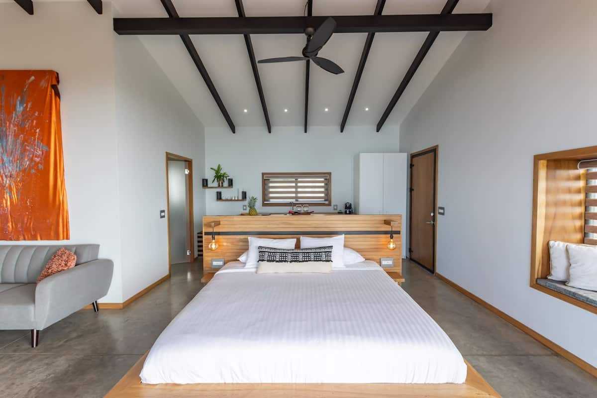 Un dormitorio moderno con una cama grande, ventilador de techo, escritorio empotrado y ventana con persianas.