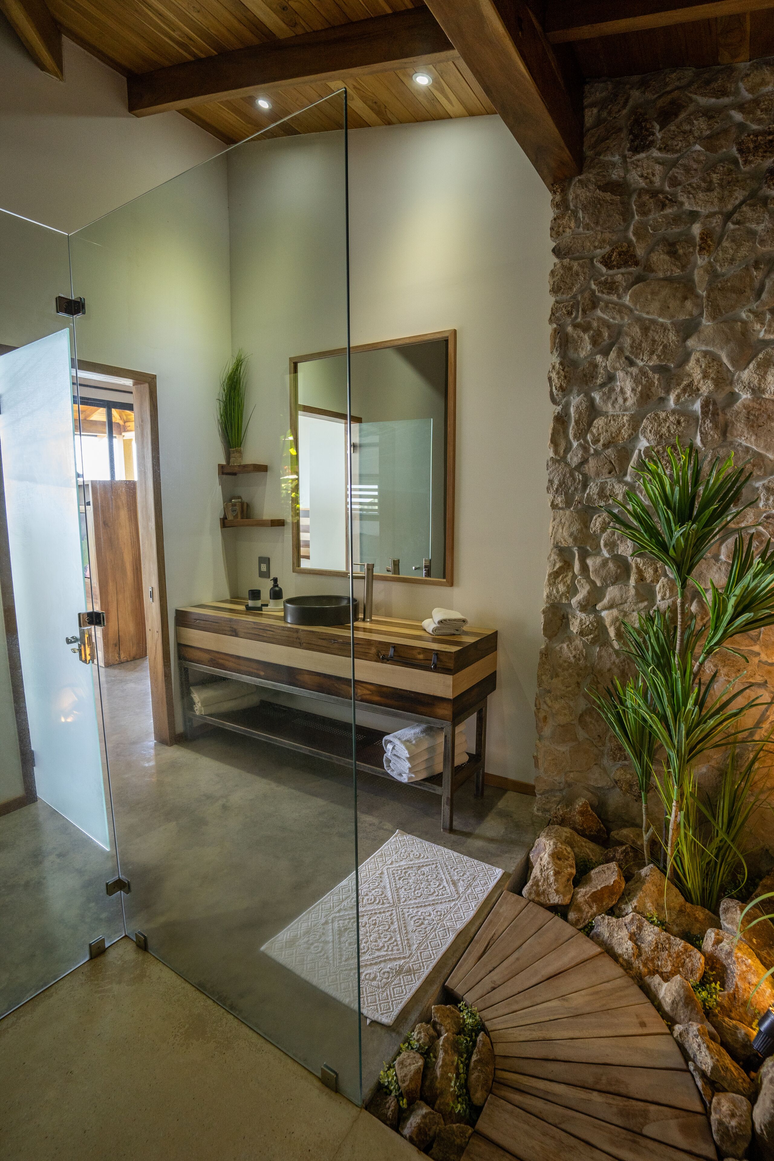 Un baño con pared de piedra, tocador de madera y cabina de ducha de vidrio.