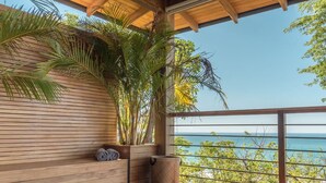 Een houten terras met uitzicht op zee, een bloempot en een opgerolde handdoek.