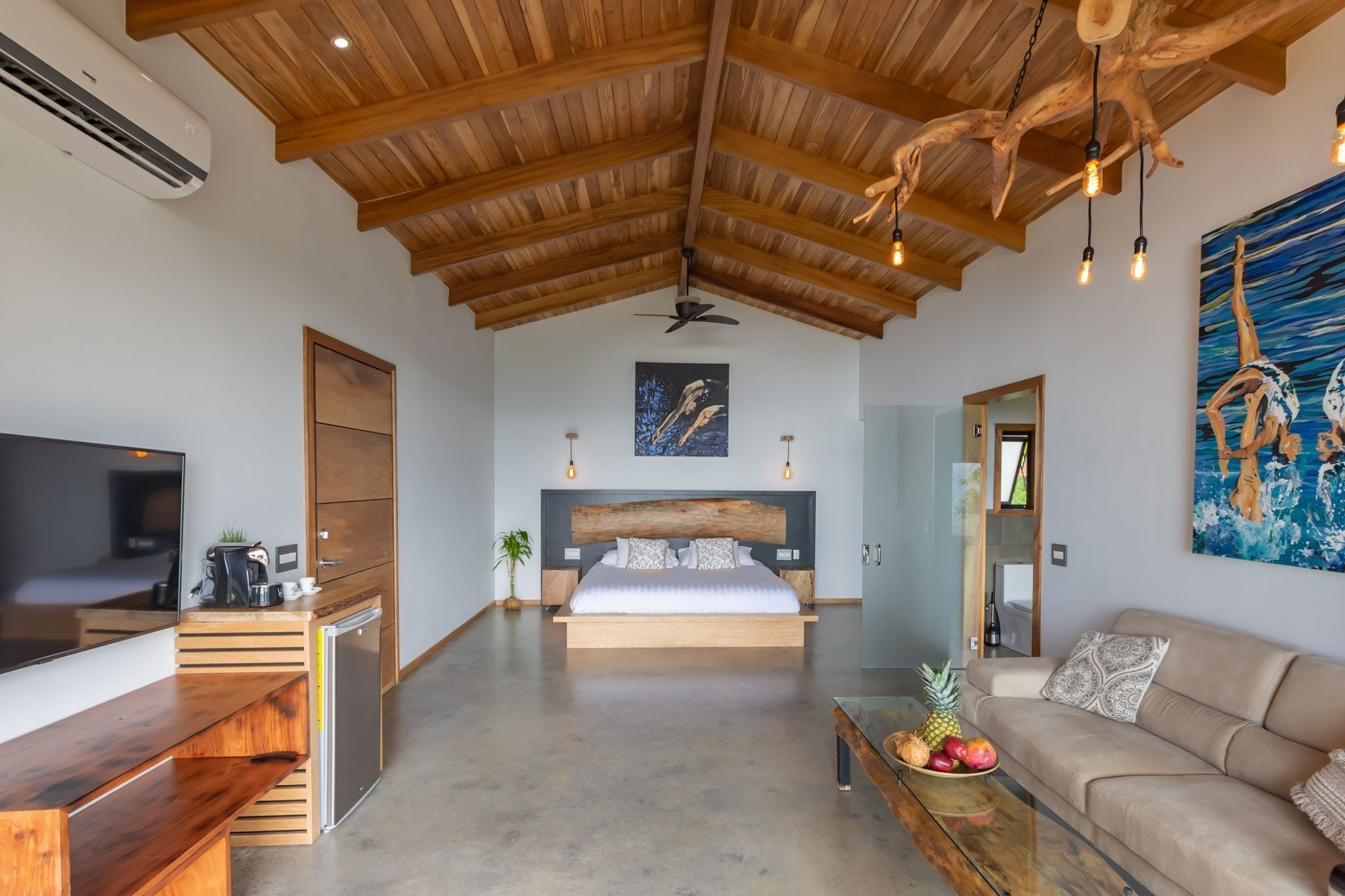 A modern bedroom with a wooden ceiling, a large bed, a TV, a desk, and a dining table with fruit.