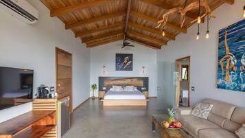 A modern bedroom with a wooden ceiling, a large bed, a TV, a desk, and a dining table with fruit.