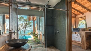 Een moderne badkamer met een douchecabine van glas, een houten wastafelmeubel en uitzicht op een buitenzwembad.