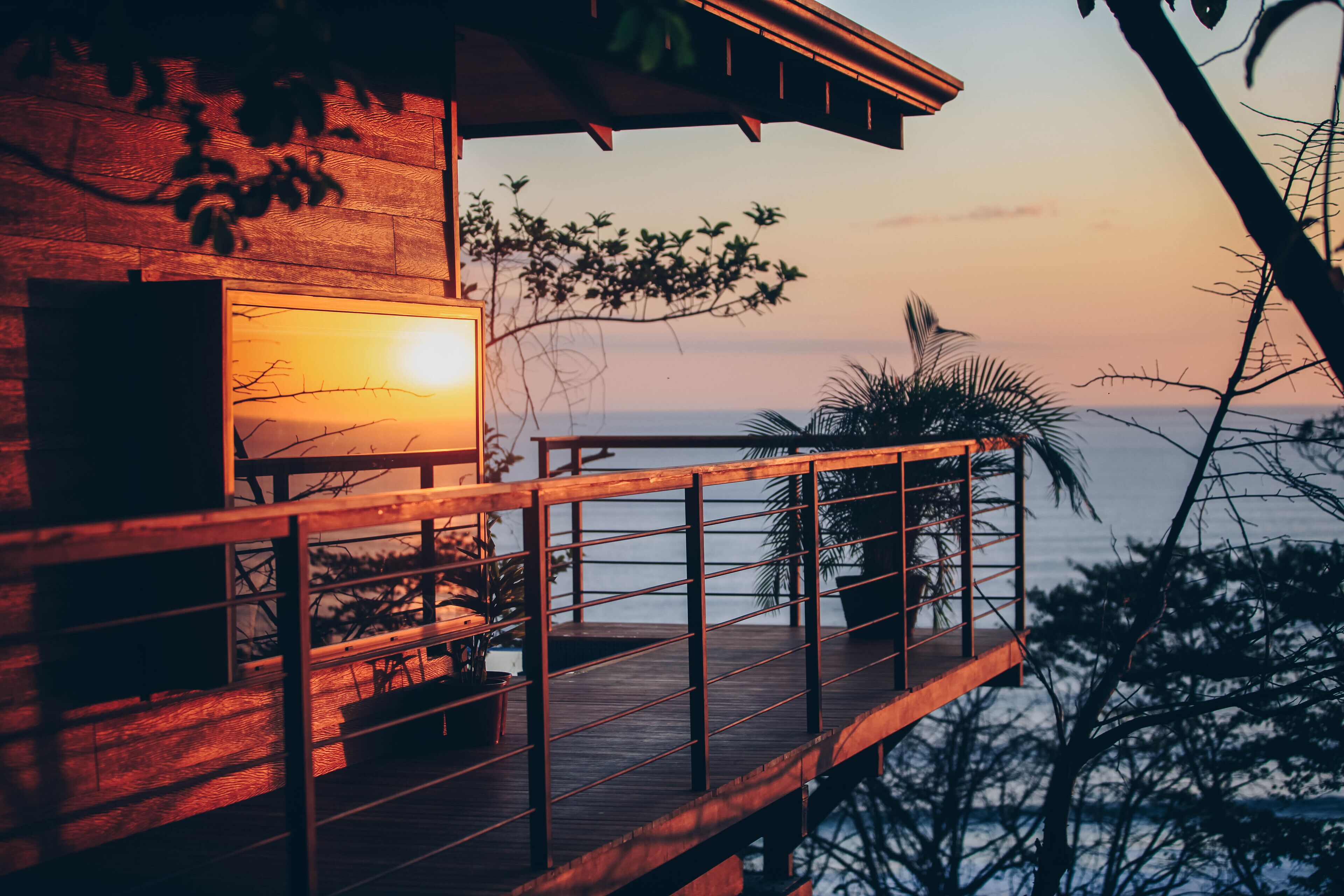 A wooden deck with a railing, overlooking a body of water, with a sunset in the background.