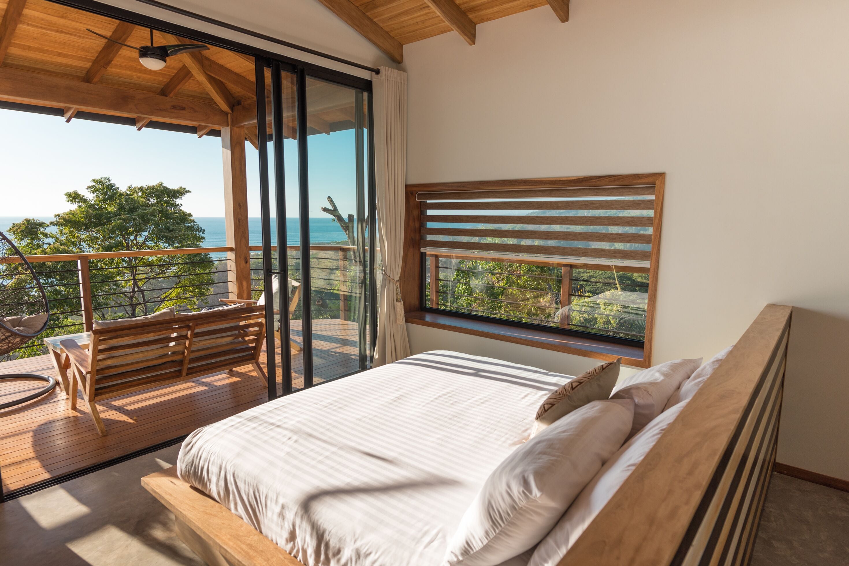 A bedroom with a large bed, a wooden bench, and a view of the sea through a window.