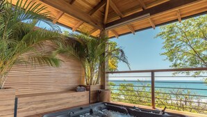 Een houten terras met een jacuzzi, houten wanden en uitzicht op de oceaan.