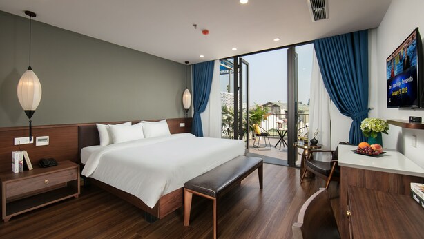 Ein Hotelzimmer mit einem großen Bett, einer Bank, einem Schreibtisch mit Blumenvase und einem Fernseher an der Wand.