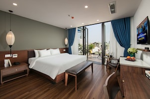 A hotel room with a large bed, a bench, a desk with a vase of flowers, and a television on the wall.