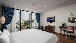 Ein modernes Hotelzimmer mit einem großen Bett, einem Schreibtisch und einem Stuhl. An der Wand befindet sich ein Fernseher und es gibt einen Blick auf die Stadt durch das Fenster.