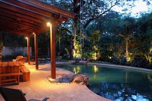 Ein Poolbereich mit einer Holzpergola, Sitzgelegenheiten und tropischer Bepflanzung.