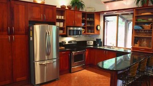 A kitchen with wooden cabinets, stainless steel appliances, a glass island table, and a window providing natural light.