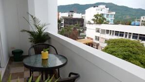 A balcony with a table and chairs, a potted plant, and a view of buildings and hills.