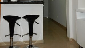 A modern kitchen with a white countertop, two black bar stools, a wooden clock, and a framed sign on the wall.