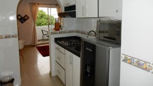 A modern kitchen with white cabinets, a black stove, a microwave, and a dishwasher. There is a red rug on the floor and a chair in the dining area.