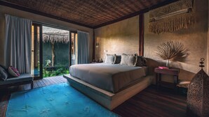 A bedroom with a large bed, a small table, a chair, a nightstand, and a decorative wall hanging. - Radhoo Tulum (Tulum)