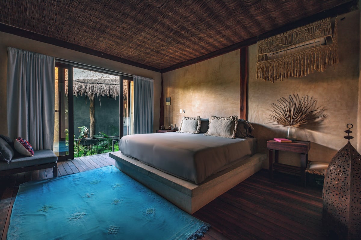A bedroom with a large bed, a small table, a chair, a nightstand, and a decorative wall hanging.