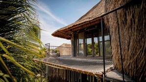 A thatched-roof building with a large window and a netted outdoor seating area. - Radhoo Tulum (Tulum)