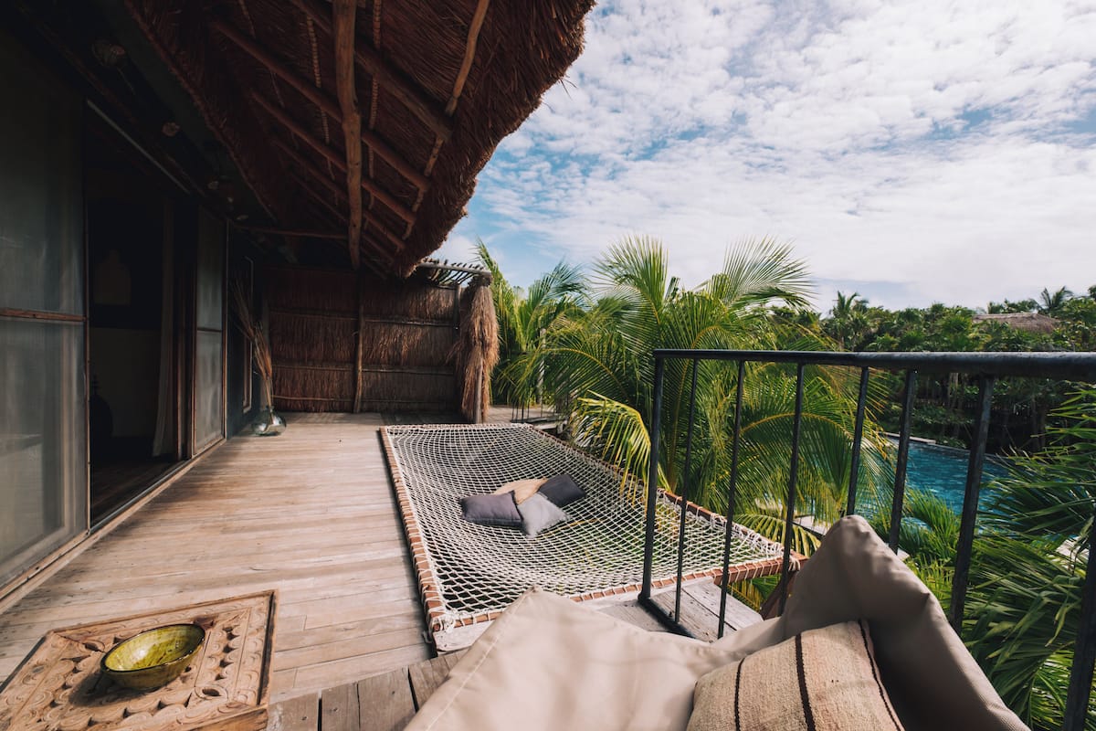 A wooden deck with a hammock, a bowl, and a view of a swimming pool and palm trees.