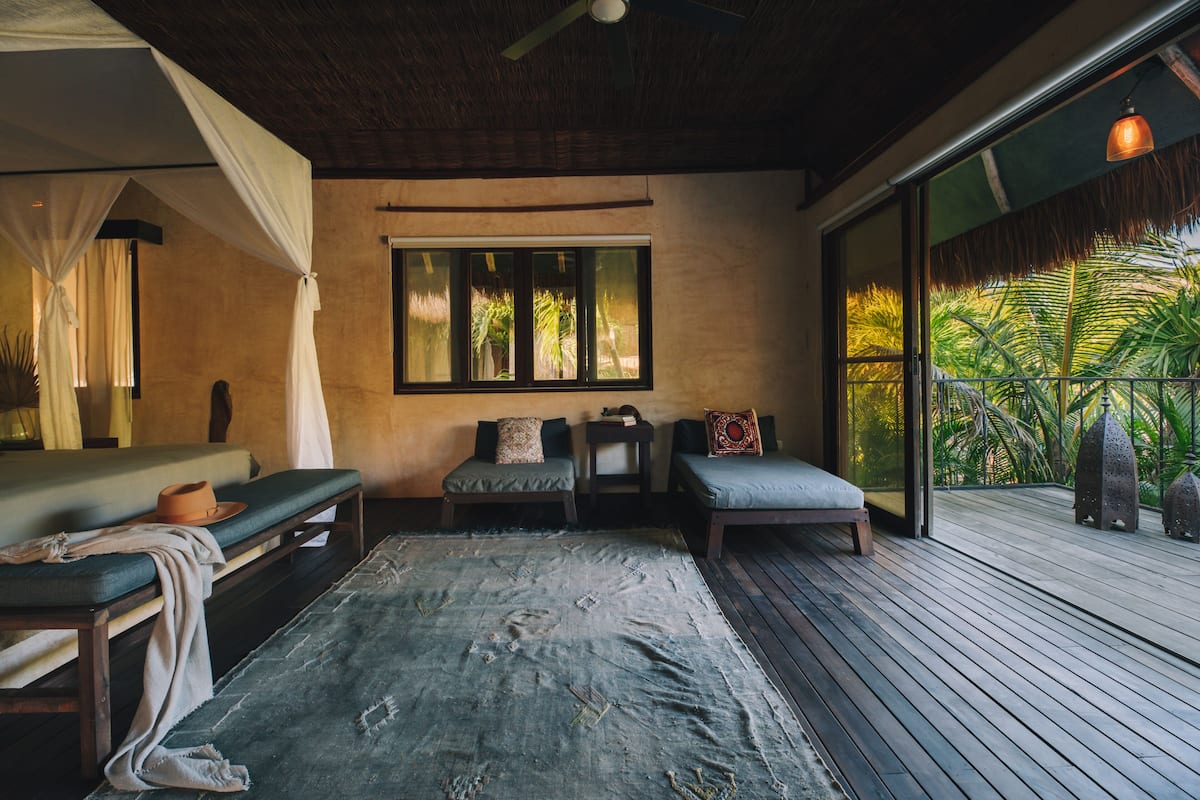 A room with a bed, two sofas, a large window, and a view of palm trees.