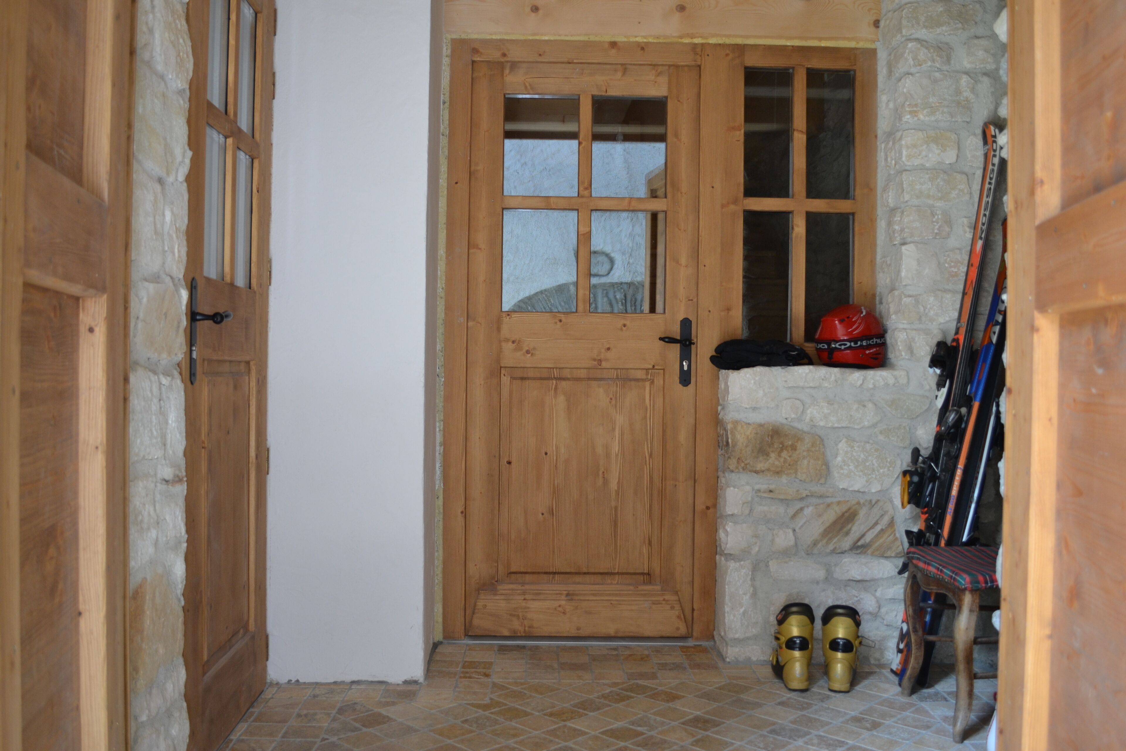 A wooden door with a stone wall and a ski rack with skis and boots.