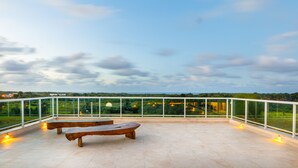 Une terrasse sur le toit, dotée de deux bancs en bois et d’une rambarde en verre, qui offre une vue sur un paysage verdoyant.