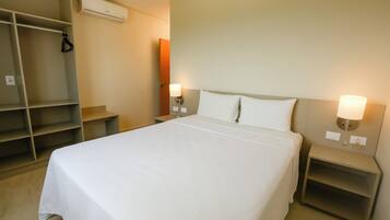 A neatly arranged hotel room with a large bed, two bedside tables with lamps, a wardrobe, and an air conditioning unit.