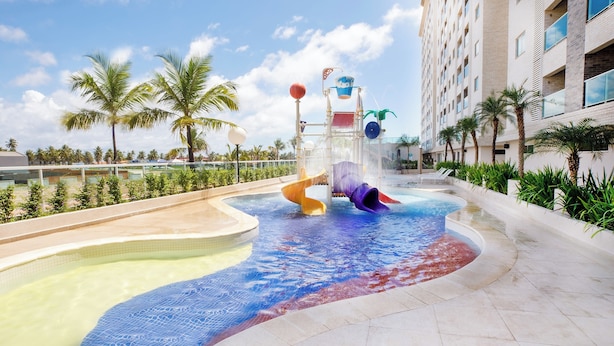 Un parc aquatique avec des toboggans et une piscine, entouré de palmiers et d’un bâtiment d’hôtel.