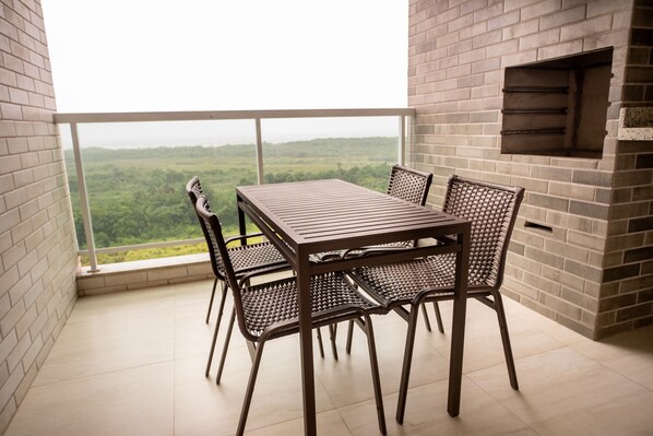 Ein Balkon mit Tisch und Stühlen, eine Backsteinmauer und Blick auf eine bewaldete Landschaft.