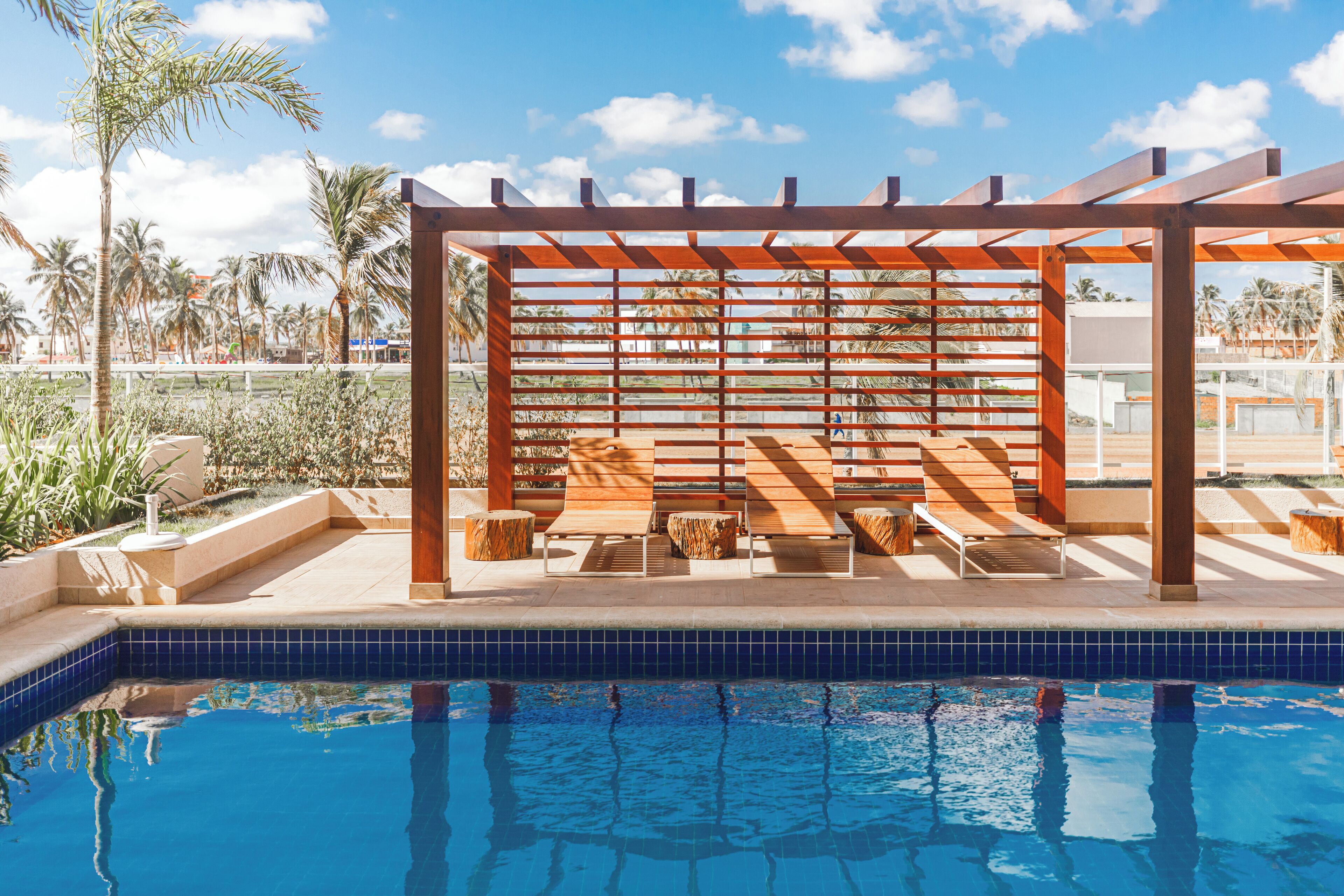 Un área de piscina con pérgola de madera y asientos, además de una piscina con azulejos.
