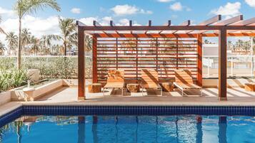 Un área de piscina con pérgola de madera y asientos, además de una piscina con azulejos.