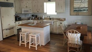 Una cocina con armarios blancos, una isla de madera, taburetes de bar y una mesa de comedor con sillas.