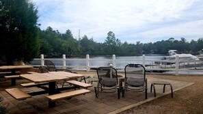 Eine Terrassennlage am Seeufer mit Picknicktischen und -stühlen, einem weißen Zaun und Booten im Hintergrund.