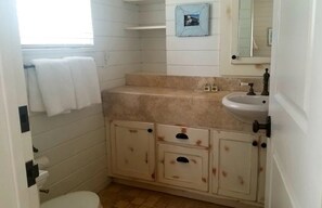 Ein kleines Badezimmer mit Toilette, Waschbecken und Schrank. Ein Fenster, an dem ein Handtuch an der Wand hängt.