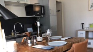 Cocina compacta con una mesa de madera, dos sillas anaranjadas, un microondas y una botella de vino.