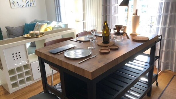 Un comedor pequeño con una mesa de madera, estanterías metálicas y un mueble blanco para guardar objetos.
