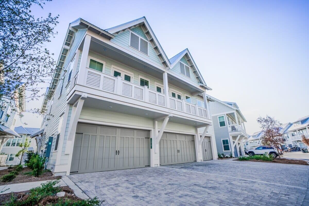Um edifício residencial de vários andares com varanda, duas garagens e um acesso pavimentado.