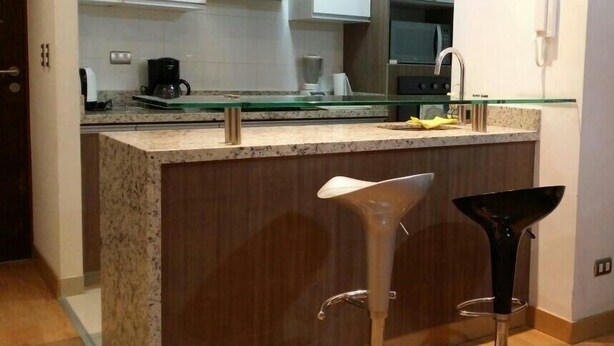 A modern kitchen with a granite countertop, stainless steel appliances, and a glass island with bar stools. - GL Apts, rent Upper Pardo Miraflores (Miraflores)
