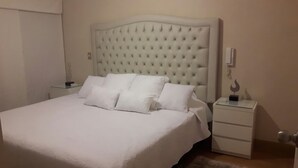 A bedroom with a large bed, white bedding, a tufted headboard, a bedside table, and a nightstand. - GL Apts, rent Upper Pardo Miraflores (Miraflores)